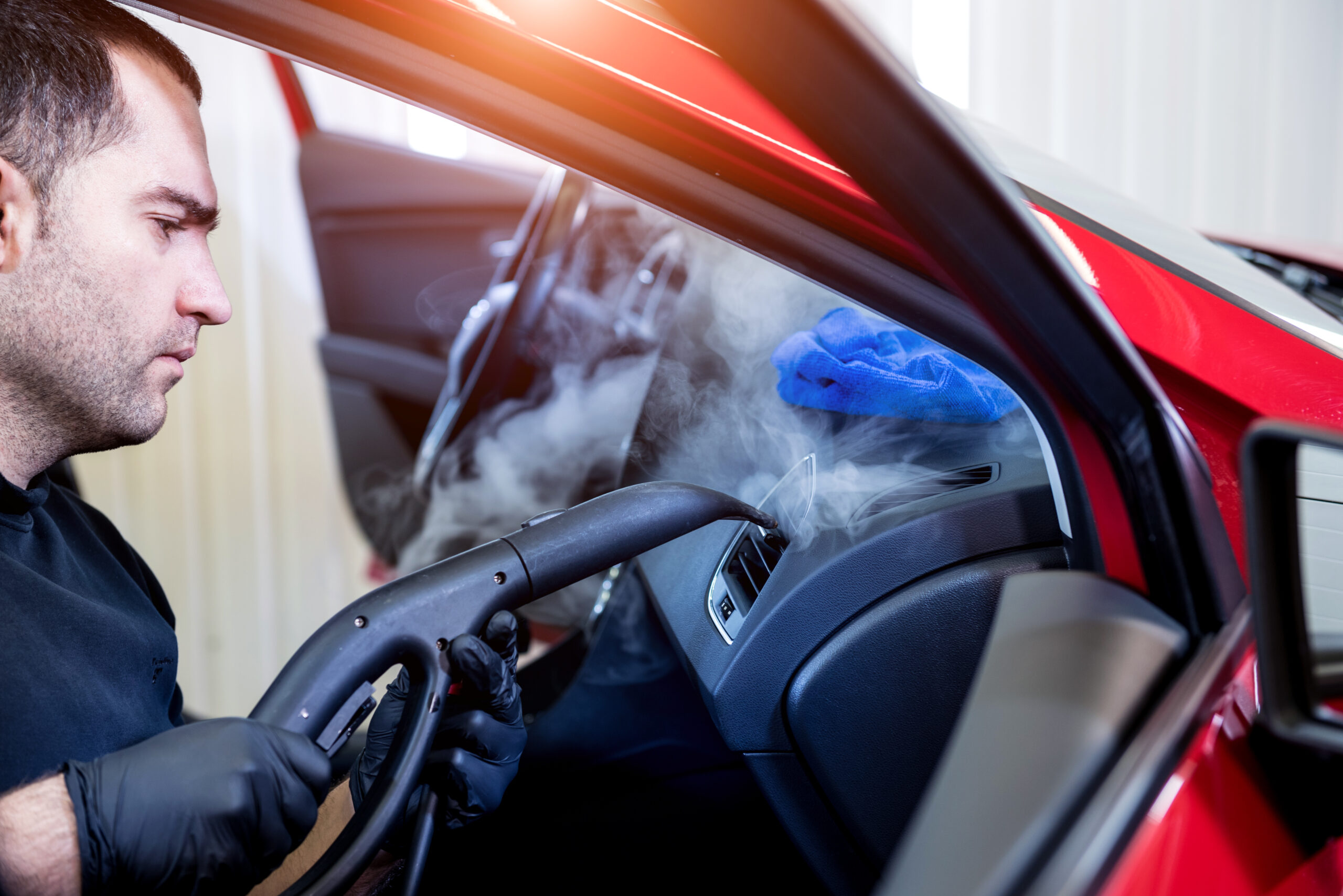 Car service worker cleans interiror with steam cleaner.