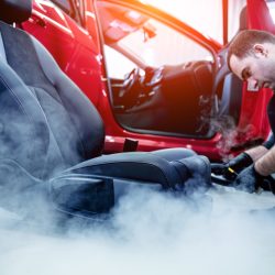 Car service worker cleaning car seat with a steam cleaner.